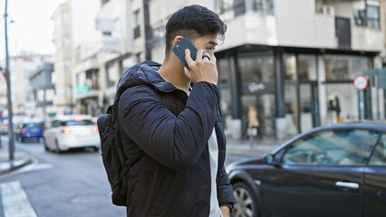 A young asian man talks on a smartphone while walking on a bustling city street.