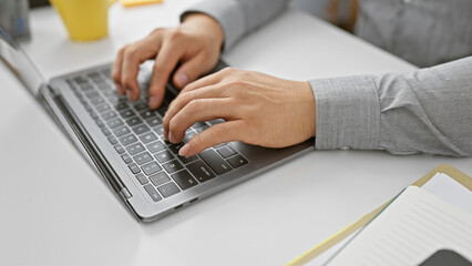 A young asian man working intently at his laptop in an office setting, focused and professional.