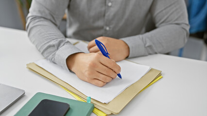 A young asian man writes down notes in a modern office setting, portraying focus and...