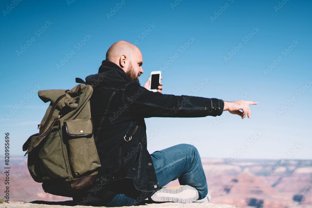 Aufkleber male traveler with backpack using good data connection for making video call sitting on rock cliff d