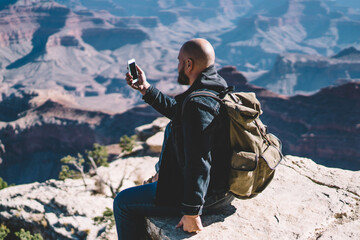 Male traveler with backpack using smartphone camera for taking picture of beautiful landscape of...