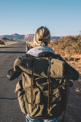 Back view of female traveler passing wild lands near asphalt road exploring southwest of USA,hipster girl enjoying active lifestyle with backpack walking on roadway having journey with hitchhiking