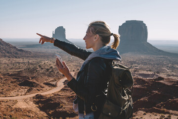 Smiling hipster girl pointing on scenery nature view in environment of Navajo reservation holding...