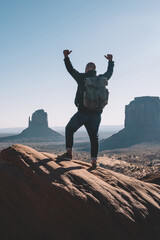 Happy male traveler feeling free standing on top of high rock ver Monument valley, back view of...