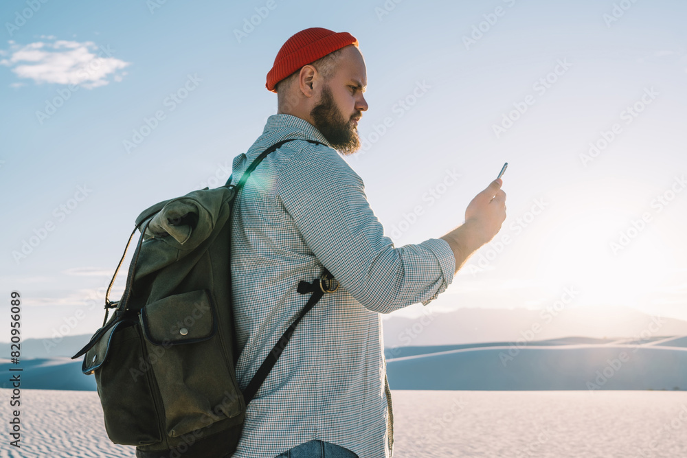 Poster serious male traveler with backpack exploring desert with white sand using navigation application on