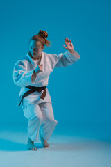 girl judoka in a white kimano with a black belt on a blue background, studio photo