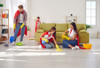 Superhero family cleaning house together. Mum, dad and children in super hero costumes and rubber...