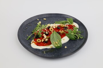 Baked peppers with feta cheese, olives and herbs on a beautiful dark plate on a white background