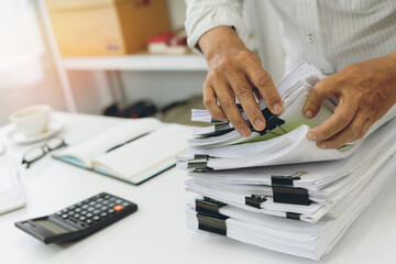 A busy office worker checking and organizing a large pile of documents at their desk.