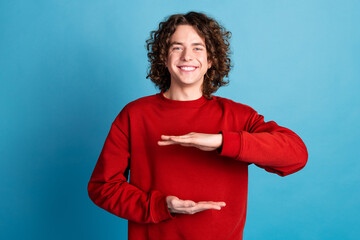 Photo of attractive funny guy wear red sweater showing arms height emtpy space isolated blue color...