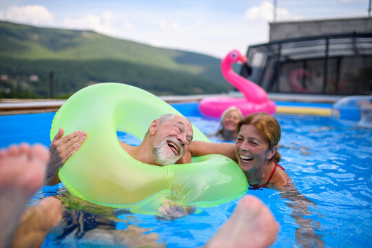 Group of cheerful seniors shaving fun in pool jumping, swiming and lounging on floats. Elderly friends spending hot day by swimming pool.