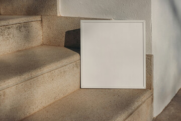 Closeup of empty square white thin picture frame leaning against wall in sunlight. Outdoor...