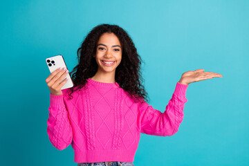 Photo portrait of lovely teen lady hold device thumb up empty space dressed stylish pink garment isolated on cyan color background