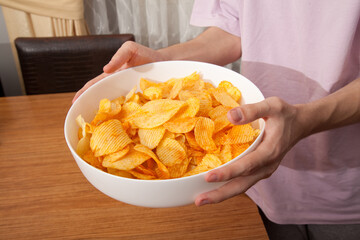 Caucasian person in pink t-shirt holding plate full of potato chips and preparing to eat