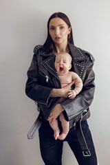 Happy mother rocker with a baby daughter stands in a leather jacket with rivets against a white...