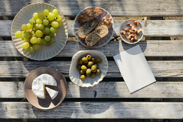 Summer food, picnic. Brie cheese, grapes fruit, olives and cashew nuts. Bread, baguette. Vintage white wooden table top view. Greeting card, invitation mockup. Free copy space, flatlay. Delicious