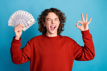 Photo of attractive funny guy wear red sweater showing money fan winking showing okey sign isolated...