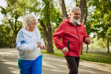 Active morning. Two people, seniors, man and woman training on warm summer morning, jogging...