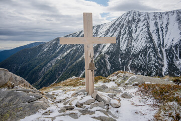 Wooden cross with a bell on a trek to Vihren peak with snowy Mount Todorka in the background.