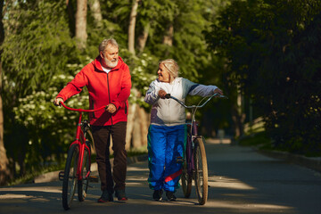 Obraz premium Senior couple, smiling, happy man and woman, joyfully bicycles through park, showing enduring spirit and love for outdoor activities. Concept of sport, aging, active and healthy lifestyle, health care