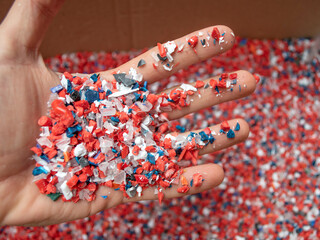 Recycled crushed plastic and a hand choosing between red and blue. Recycling and reuse of plastic. The problem of environmental pollution. Ecology and innovations. Various types of plastic.