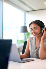 Woman Wearing Headset Sitting At Desk With Laptop Working In Office Call Centre Team Taking Call