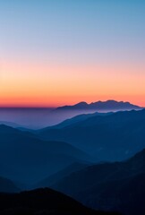 A breathtaking sunrise over the mountains, casting an orange and blue glow on their silhouette against a clear sky.