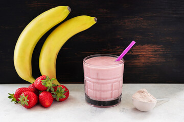 Strawberry and banana smoothie, protein drink in a glass, measuring scoop with whey protein powder,...