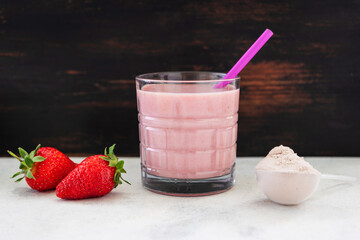 Strawberry smoothie, protein drink in a glass, measuring scoop with whey protein powder, blended...