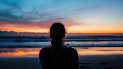 Fototapeta premium Silhouette of a woman looking at the beach and the ocean at sunset from behind.