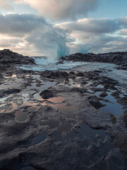Vertical photo of a wave breaking in the background and small pools of water in the foreground