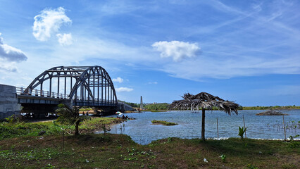 Obraz premium View of the estuary towards the sea with a bridge and a mangrove forest conservation area with a cloudy blue sky.