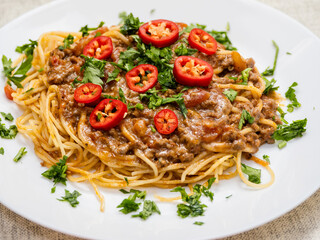 A plate of spaghetti with meat sauce and tomatoes. The plate is on a wooden table. The dish looks delicious and inviting. Italian style meal made with high quality product.