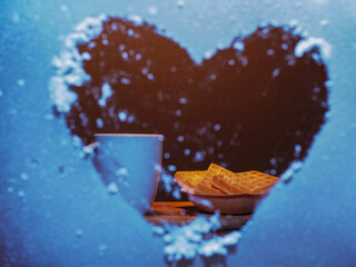 A heart-shaped window with a white cup and a plate of waffles. The waffles are in a bowl and the...