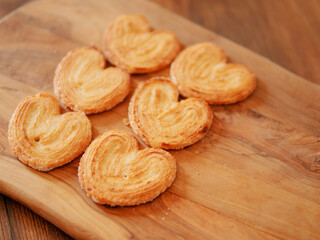 Delicate cookies made in heart shape on wooden board underneath. French style pastry sweet desert. Bakery product. Selective focus. Warm color. Tasty treat for tea or coffee