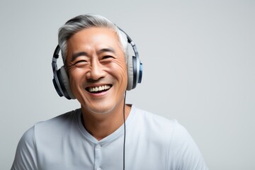 Portrait of a blissful asian man in his 50s listening to music in minimalist or empty room...