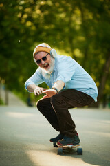 Elderly skateboarder cruises down park pathway, with headphones on, in stylish sunglasses and...