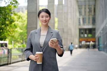 Confident Businesswoman Walking Outdoors with Coffee and Smartphone