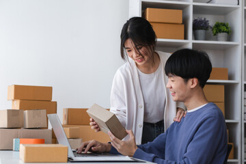 A happy Asian online shopping entrepreneur couple takes orders and packs products to send to...