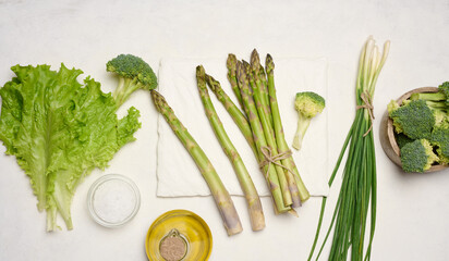 Raw asparagus, broccoli and spices on white background, top view.