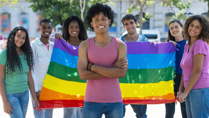 Laughing brazilian male young adult with LGBTQ rainbow flag and group of international people