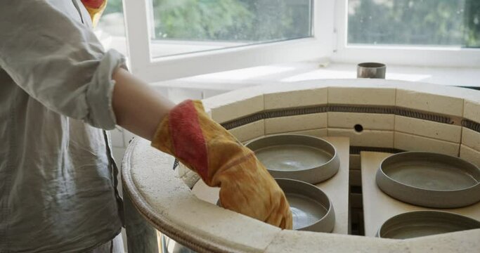 Potter Removing Baked Ceramic Plates from Kiln in Workshop