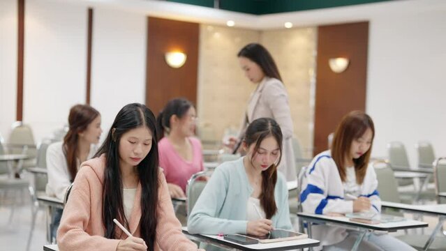 A group of girls are sitting in a classroom and writing. Scene is focused and studious