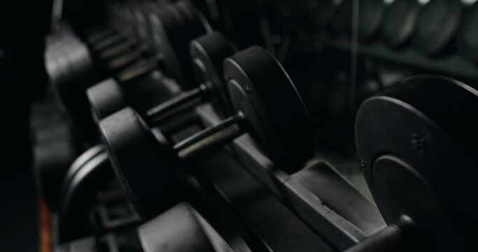 Close-up shot of a focused athlete's hand selecting dumbbells from a gym rack, illustrating dedication and strength in fitness training. Focused Athlete Preparing for Workout Selecting Dumbbells