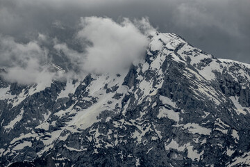 Alpine peaks rise through clouds, their jagged summits shrouded in mist. The scene captures the...