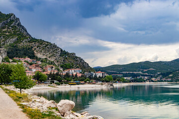 A picturesque small town lies peacefully along the serene shore of a beautiful lake, under a vast...