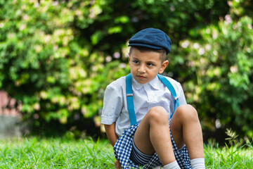 little Latino boy sitting on the ground in the park, looking to the side a bit angrily