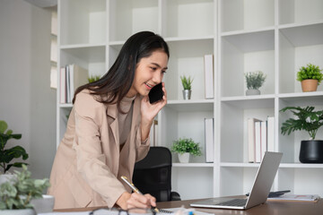 Obraz premium Asian businesswoman talking on the phone, having an online business meeting in a modern home office.