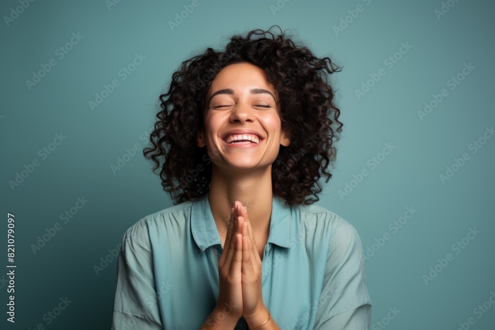 Wall mural portrait of a joyful woman in her 30s joining palms in a gesture of gratitude in front of solid colo - Wall murals