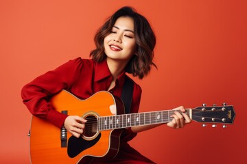 Portrait of a tender asian woman in her 40s playing the guitar in solid color backdrop